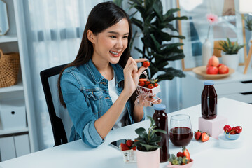 Smiling young beautiful Asian reviewing tasty mixed strawberry and cherry juice detox drinks,...