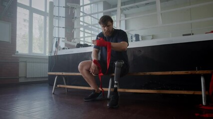 Bearded male athlete with prosthetic leg uses hand wrap in gym - Powered by Adobe