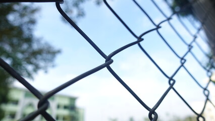 A wire fence in focus against with a blue sky. Symbolizes barriers, boundaries, and separation while offering a conceptual view of security and enclosure.