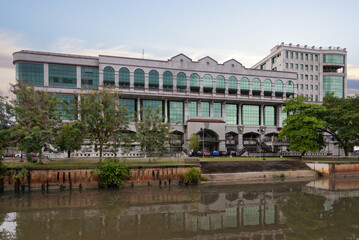 Mall Gadong stands prominently by the river in Bandar Seri Begawan, Brunei, featuring modern architecture and lush palm trees. Visitors enjoy shopping and leisure activities in this bustling complex