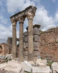 Obraz premium Historic ruins featuring three ancient columns with ornate capitals and stone walls at Ephesus, Selcuk, Turkey. Archaeological site under cloudy sky