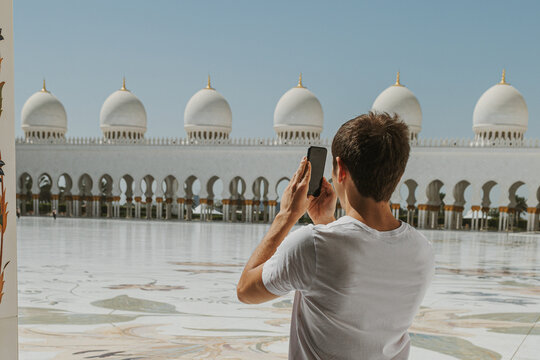 Tourist taking photo of Sheikh Zayed Grand Mosque domes in Abu Dhabi on a sunny day
