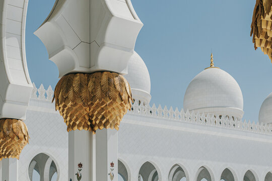 White domes and golden palm columns at Sheikh Zayed Grand Mosque under clear blue sky
