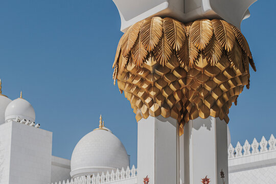 White domes and golden palm columns at Sheikh Zayed Grand Mosque under clear blue sky
