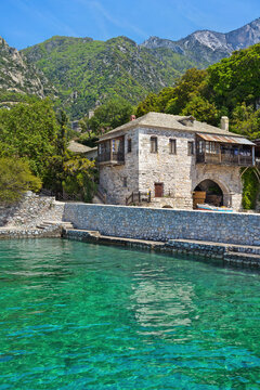 Stone-built harbor ("arsanas") of Agios Pavlos Monastery, Mount Athos, with turquoise waters and green hills in the background, a serene and sacred coastal landscape.