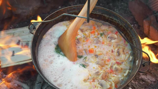 Fragrant, creamy broth of a mushroom soup, simmered over a campfire, is enhanced with herbs, creating a delightful culinary experience. Top view. Close up.