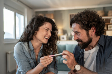Happy couple holding positive pregnancy test at home