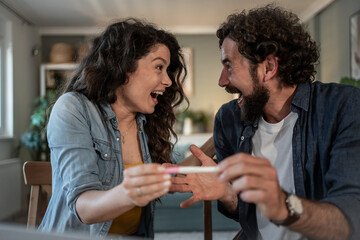 Happy couple celebrating positive pregnancy test result at home