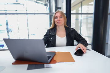 Confident young woman working on laptop in a modern coworking space with natural light and plants.