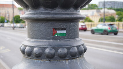 A small Palestinian flag sticker is affixed to a weather-worn metal lamppost