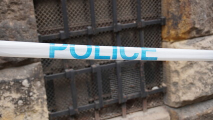 white blue police tape is stretched taut around a multi-storey urban building, cordoning off the area as an active crime scene