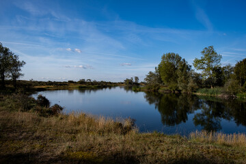 Peaceful view of a calm lake surrounded by natural scenery, with smooth reflections dancing on the water’s surface. Whether framed by forest, mountains, or open sky, the lake evokes a sense of
