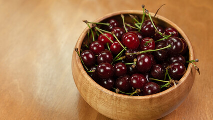 Fresh cherries in a wooden bowl on a natural wood surface during a summer afternoon