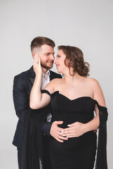 Beautiful pregnant young girl in a black long dress with her husband on a white background in a photo studio. Pregnancy.