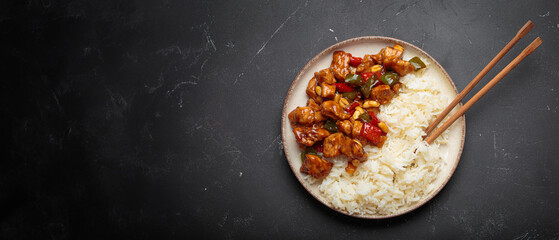 Steaming Chinese kung pao chicken with rice, veggies, and peanuts in spicy sauce. Top view on dark...