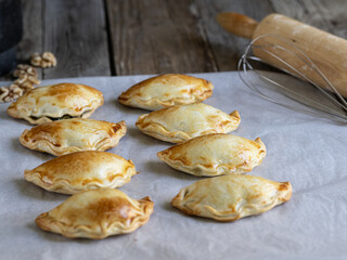 Photograph of freshly made vegetarian dumplings on baking paper and with kitchen utensils and ingredients around, on a rustic wooden table
