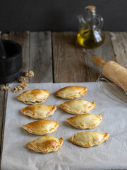 Photograph of freshly made vegetarian dumplings on baking paper and with kitchen utensils and ingredients around, on a rustic wooden table