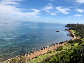 Coastal bluff view overlooking calm blue ocean waters and rocky shoreline under a sunny sky.