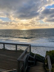 Obraz premium Wooden deck facing the ocean at dusk with gentle waves and dramatic clouds.