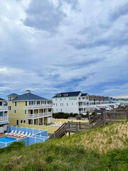 Seaside cottages with ocean views on a grassy hill, bathed in sunlight under scattered clouds.