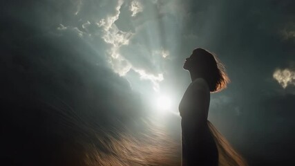 Silhouette of a woman gazing upwards into sun rays piercing through dramatic storm clouds, conceptualizing hope and inspiration, shot from below.