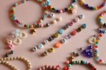 Friendship bracelet spelled with letter beads. Colorful handmade bracelets and various beads. Selective focus, pink background.