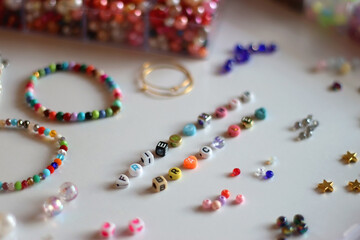 Friendship bracelet spelled with letter beads. Colorful handmade bracelets and various jewelry making supplies. Selective focus, white background.