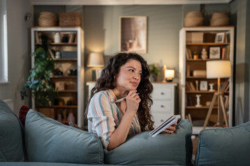 Woman relaxing on sofa writing in notebook at home
