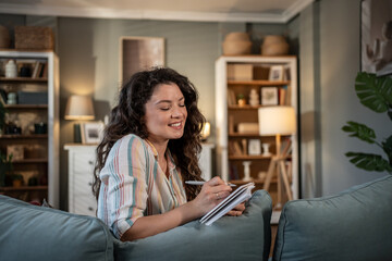 Obraz premium Young woman writing on notebook sitting on sofa at home