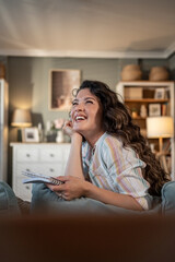 Cheerful woman holding notebook and laughing on sofa at home