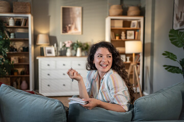 Obraz premium Young woman taking notes and smiling on sofa at home
