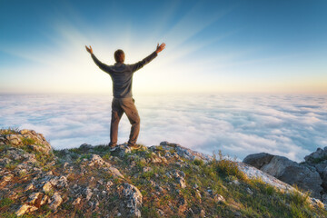 Man stands over the cover clouds on the edge of the abyss and looks on sun.