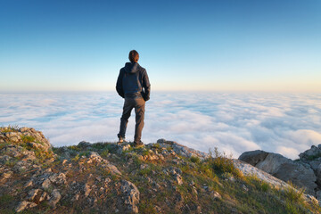 Man stands over the cover clouds on the edge of the abyss and looks on sun.