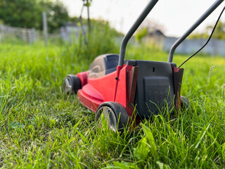 Red lawn mower cutting green grass in garden during summer day