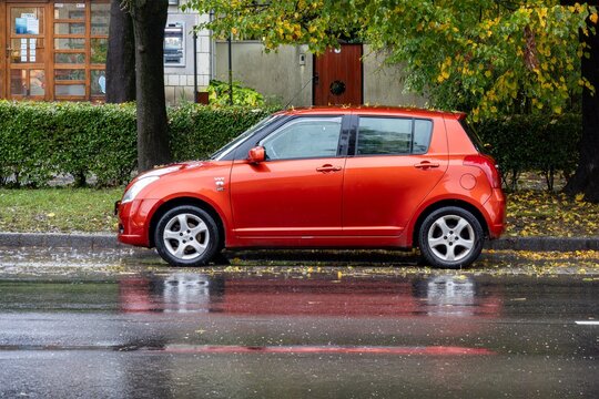 Side view of red Suzuki Swift RS hatchback car in rain parked on street
