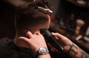 Close-up of a professional barber using electric clippers to trim a male client's haircut with precision. The client’s hair is sectioned with clips in a modern barbershop setting..