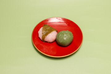 緑背景の菓子皿にのせた草餅と桜餅