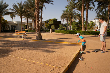 Man and boy playing petanque in hot country, father and son in hotel playing on sand
