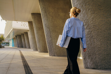 A businesswoman walks confidently in a modern city, showcasing her professional style