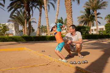 Man and boy playing petanque in hot country, father and son in hotel playing on sand