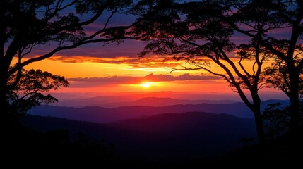 Fototapeta premium Majestic sunset over mountain range framed by trees. A vibrant sunset paints the sky in hues of orange, purple, and pink over a mountain range, with silhouette trees framing the view