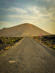 Empty road heads straight toward a towering volcanic mountain in Lanzarote. Rugged terrain and soft...