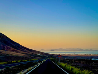 Scenic view of Fuerteventura while driving along a road that curves downhill toward the ocean at...
