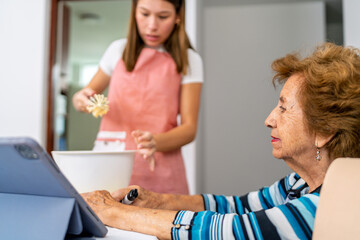 Grandmother learning baking online while granddaughter is whisking
