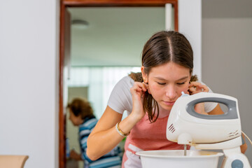 Young baker whisking ingredients with electric mixer, grandmother watching