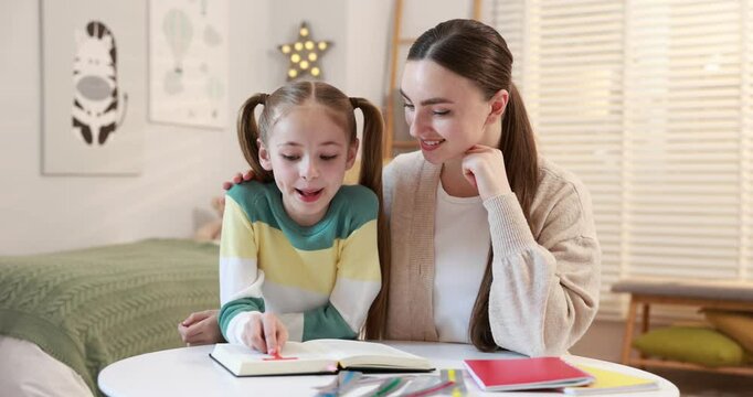 Dyslexia. Mother and her daughter reading book at table indoors