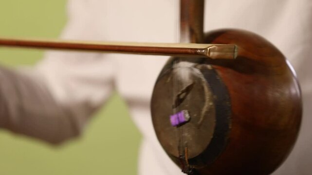 A close-up shot captures a musician's hands skillfully playing a traditional kamancheh, a spike fiddle, drawing the bow across its strings in a dynamic and focused musical performance.