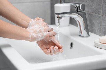 Woman washing hands at sink in bathroom, closeup