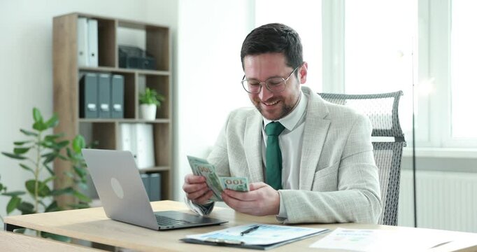 Greedy banker counting money and smiling at table in office