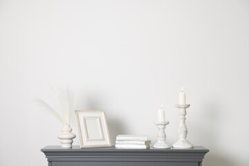 Stylish candlesticks with burning candles and other decor on fireplace near white wall indoors
